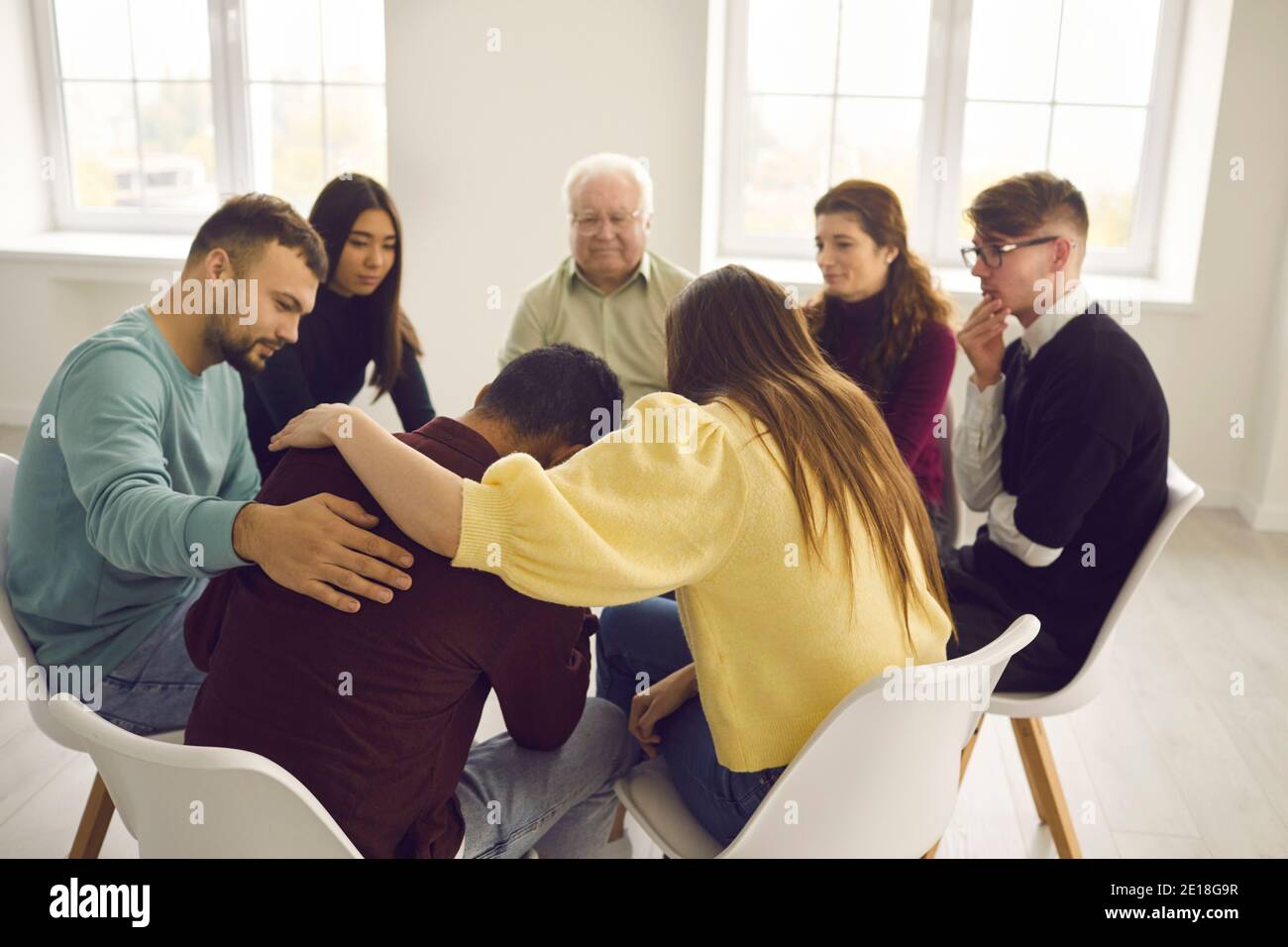 Diverse people supporting and comforting a desperate man in a group therapy session Stock Photo