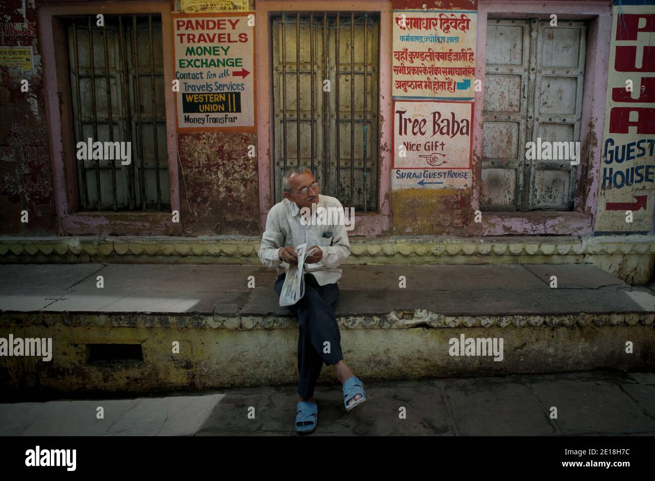 A senior citizen holding a newspaper, sitting on concrete platform in front  of a building painted with colourful advertisements in Varanasi, Uttar  Pradesh, India. © Reynold Sumayku Stock Photo - Alamy