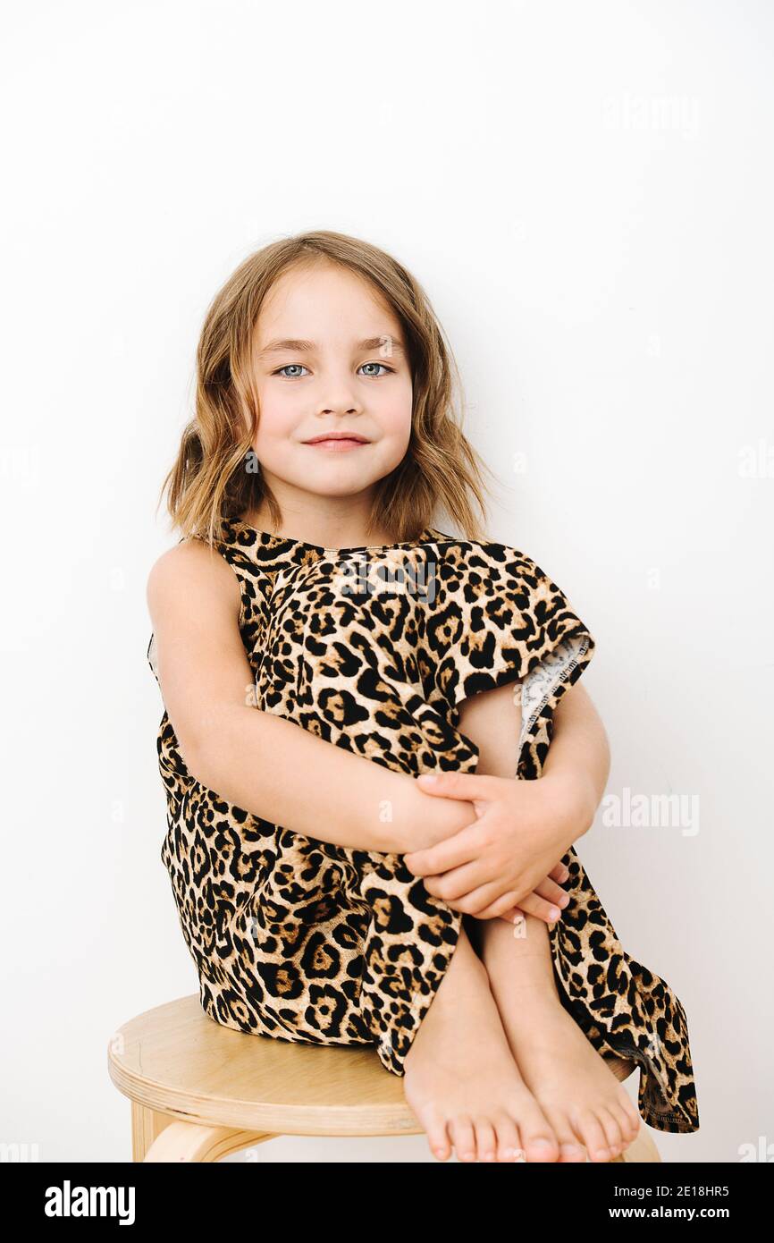 Portrait of a girl, she sits hugging her knees in a leopard print dress ...