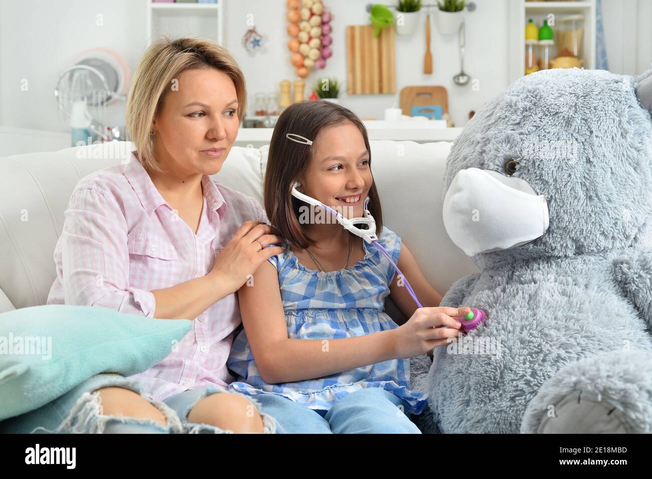 Girl and mother playing with toy bear in facial mask. Girl with stethoscope Stock Photo