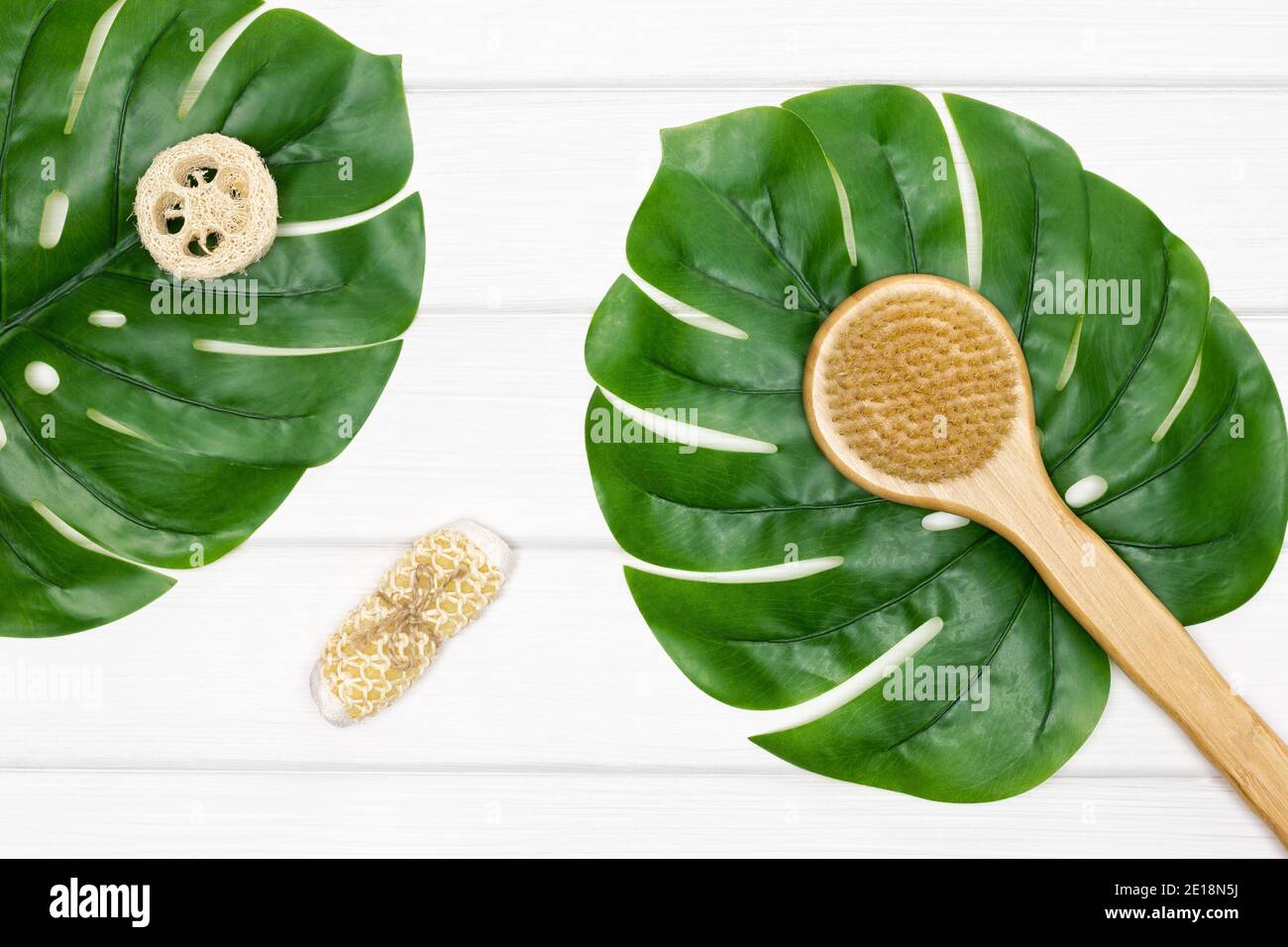 Body brush, loofah, scrubber with green leaves on white painted wooden