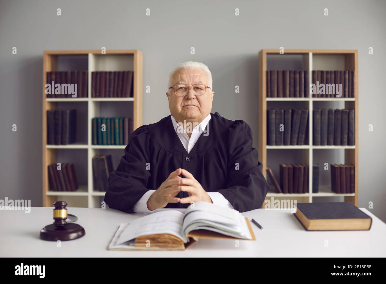 Wise mature judge sitting at desk with open Code of Law in his office or courtroom Stock Photo
