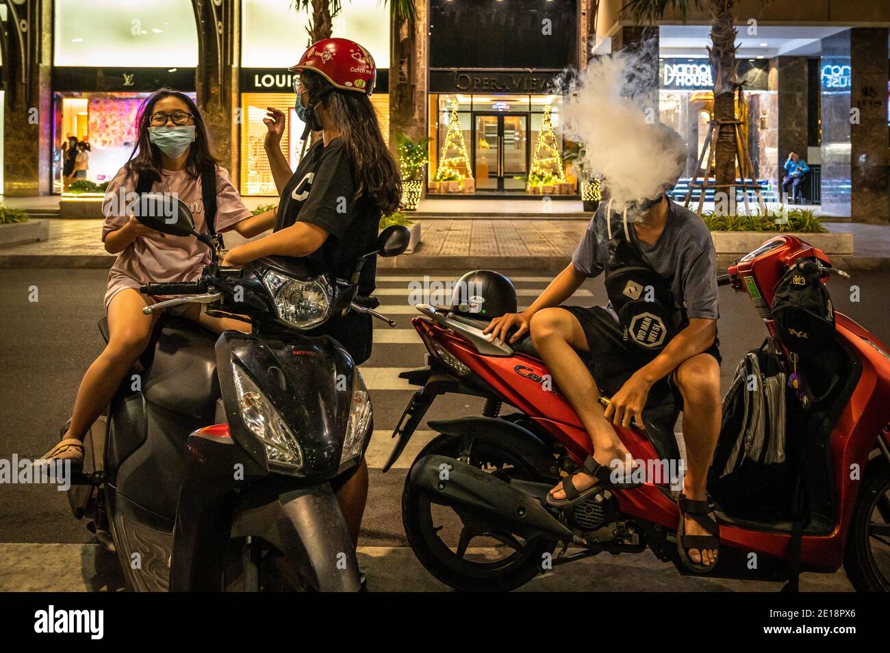 Young man smoking while two girls talk while hanging out in the center in Ho Chi Minh City, Vietnam Stock Photo
