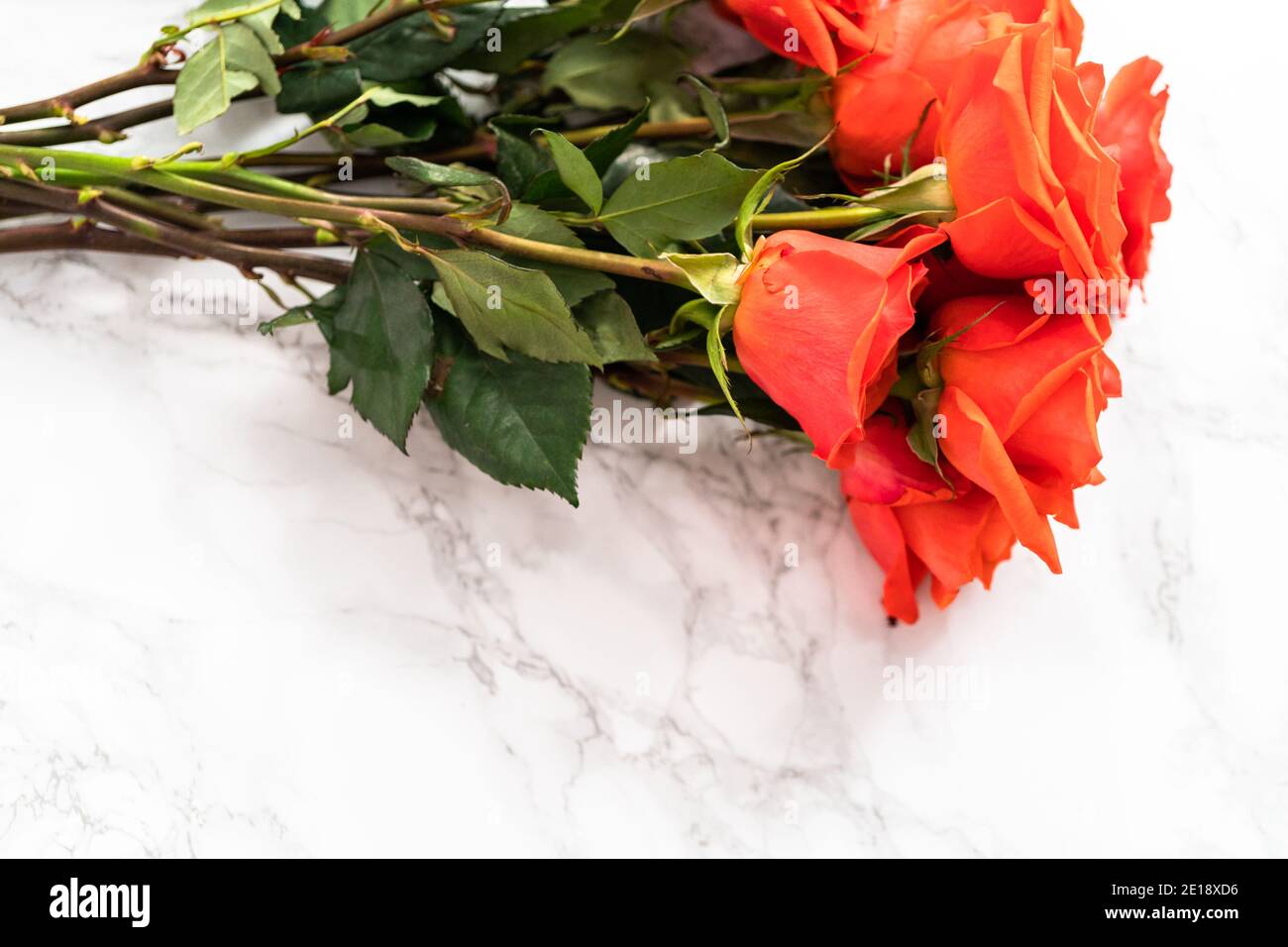 Arranging red roses and green leaves into a bouquet on a marble ...