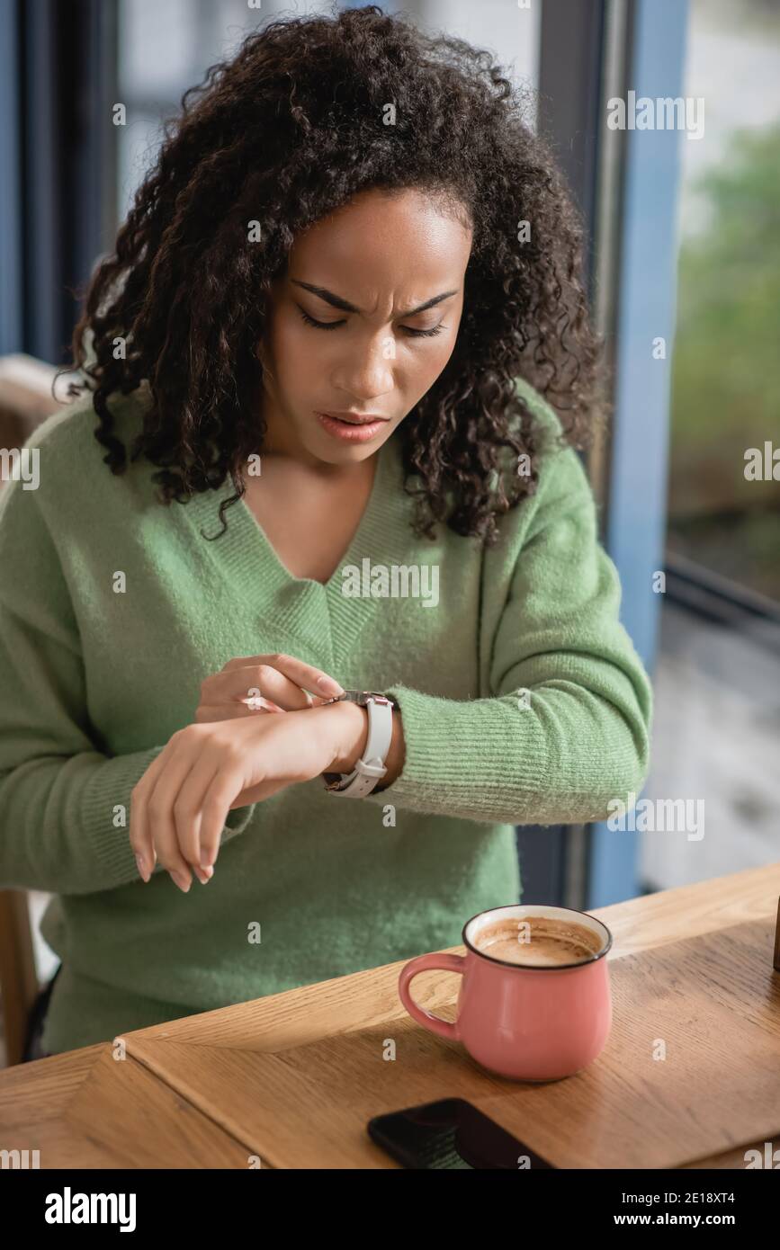 worried african american woman checking watch on wrist while waiting in