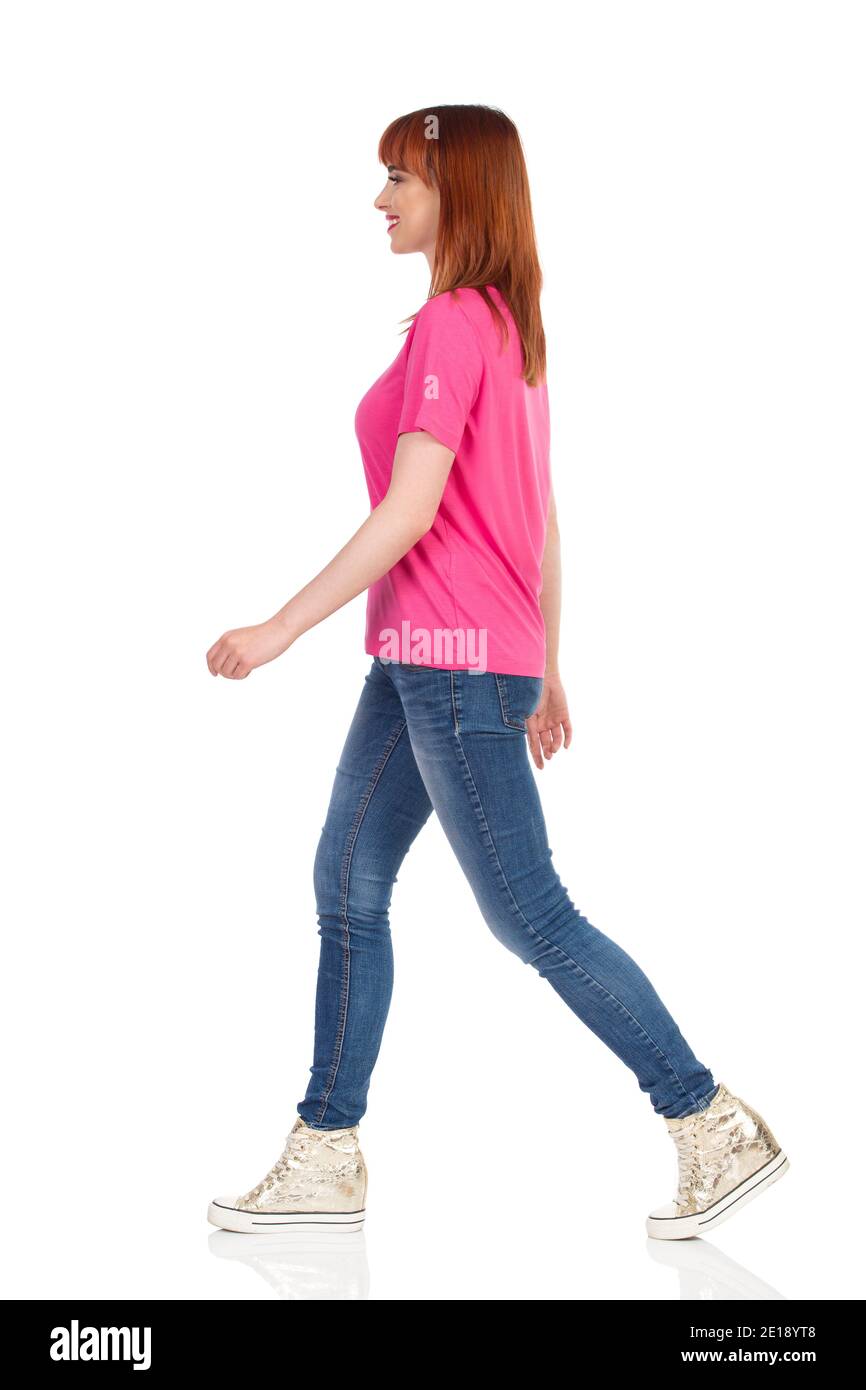 Happy casual young woman is walking, looking away and smiling. Side view. Full length studio shot isolated on white. Stock Photo