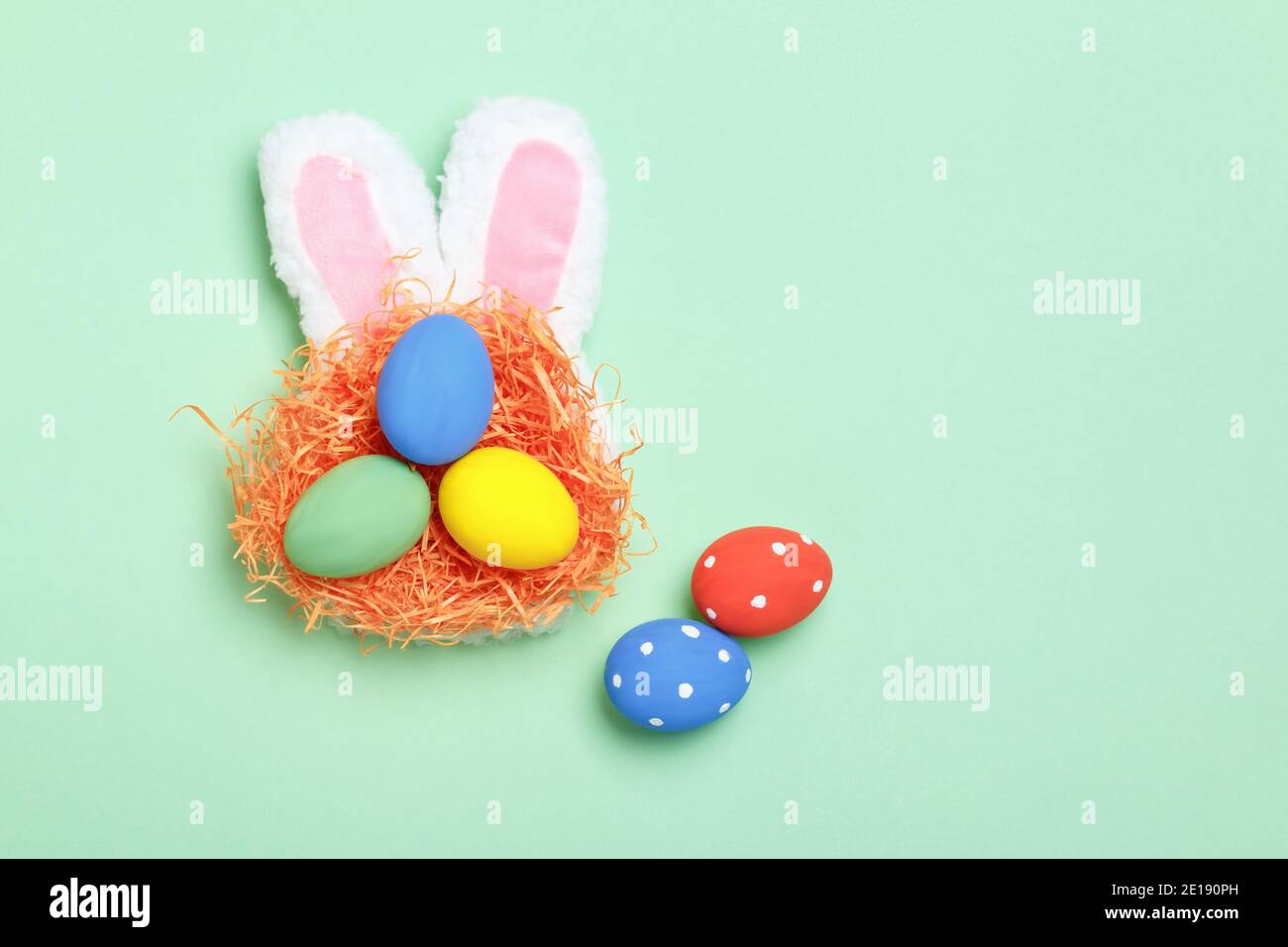 Easter eggs in a nest, bunny ears on a mint green background. Greeting card with copy space flat lay. Stock Photo