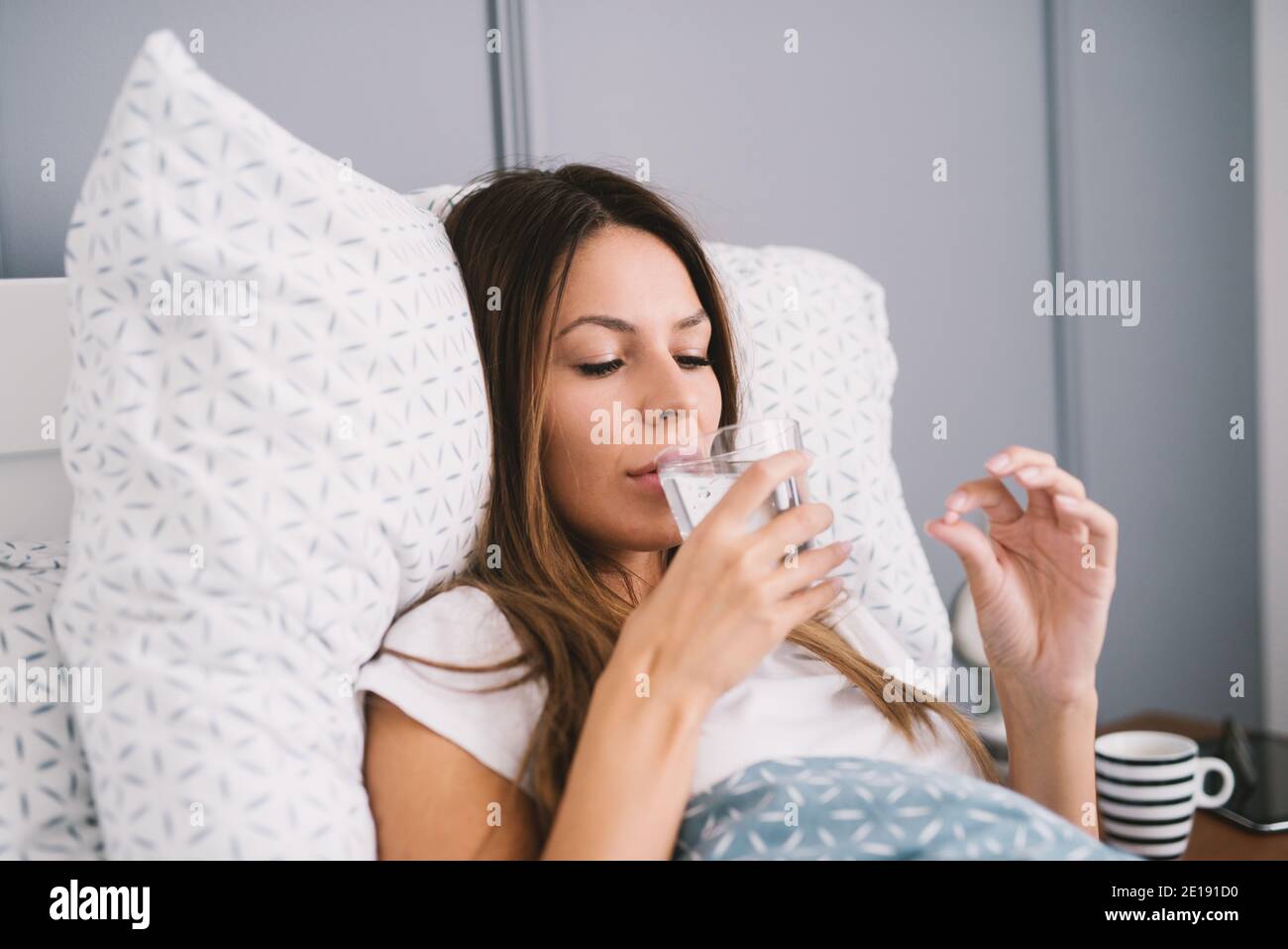 Beautiful young woman drinking water while lying in the bed Stock Photo