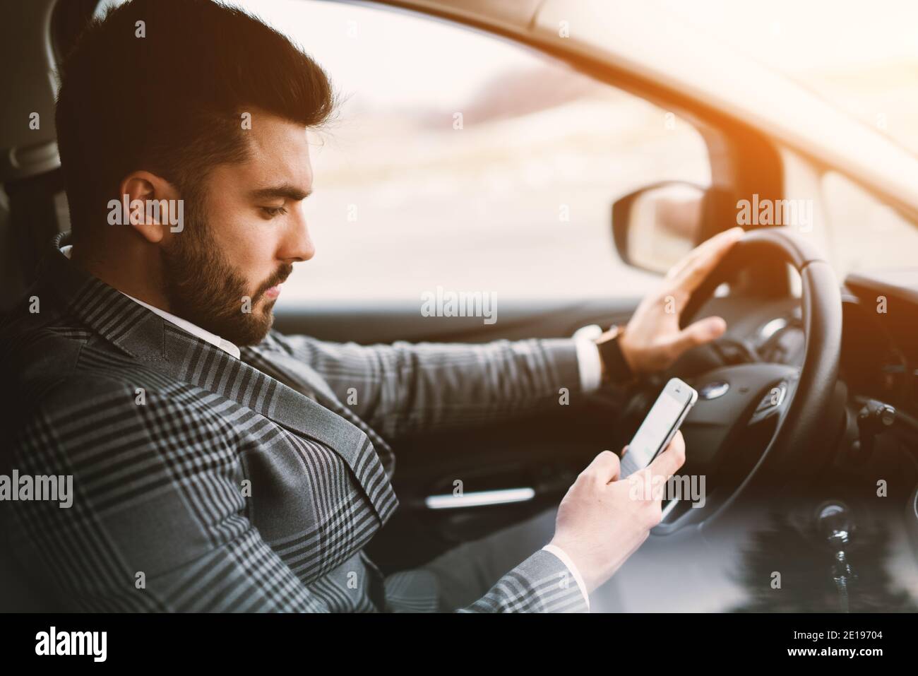 Handsome suited man with beard texting while driving a fancy car on a street. Stock Photo