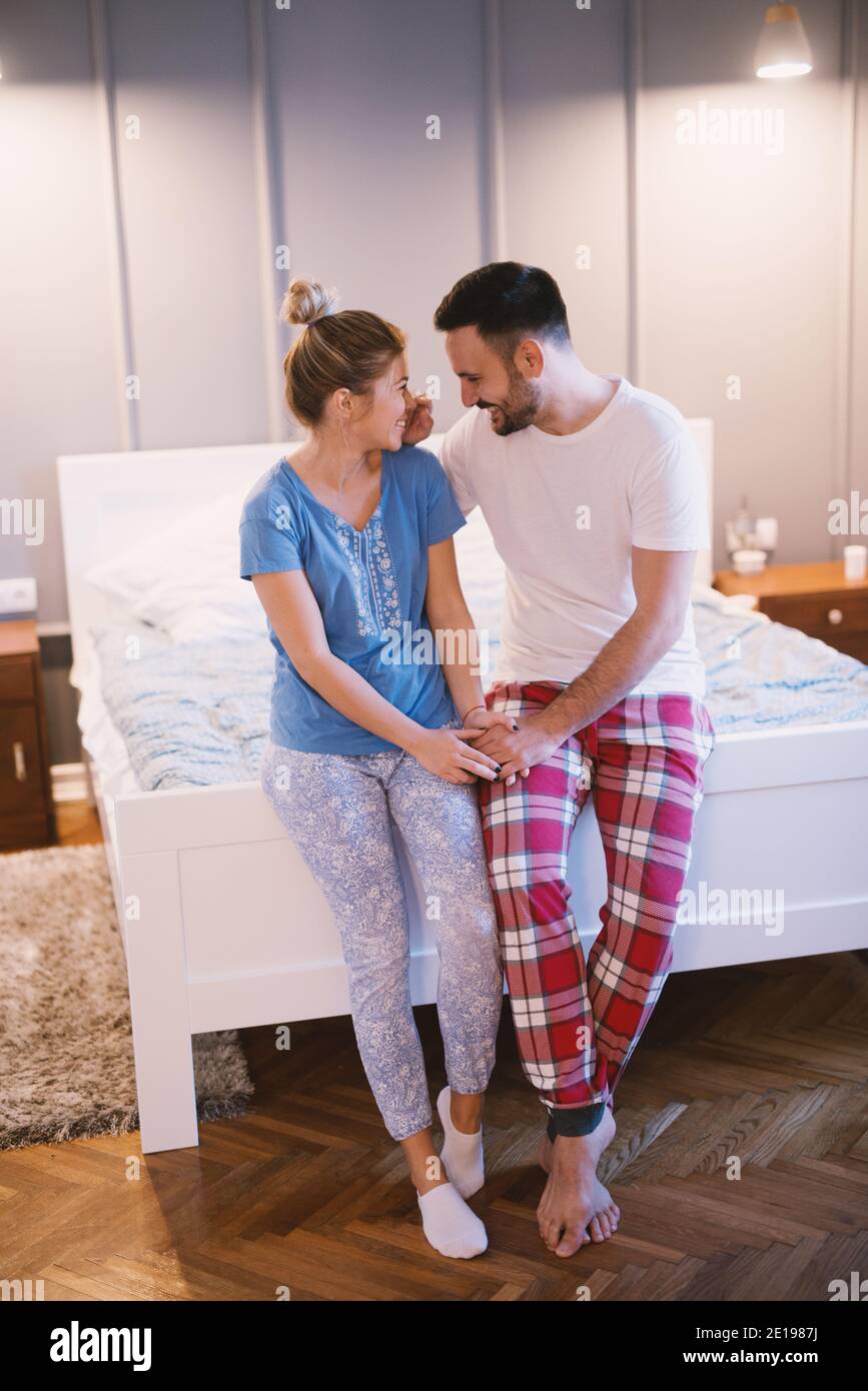 Cheerful happy romantic couple sitting on the edge of the bed at night and  cuddling. Relationship and weekend goals Stock Photo - Alamy