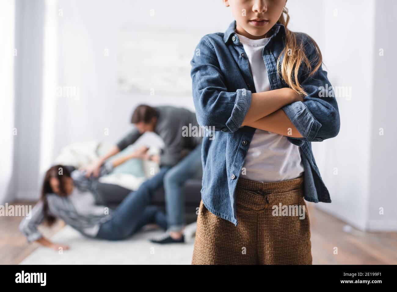 Girl with crossed arms standing near abusive father beating mother at home on blurred background Stock Photo