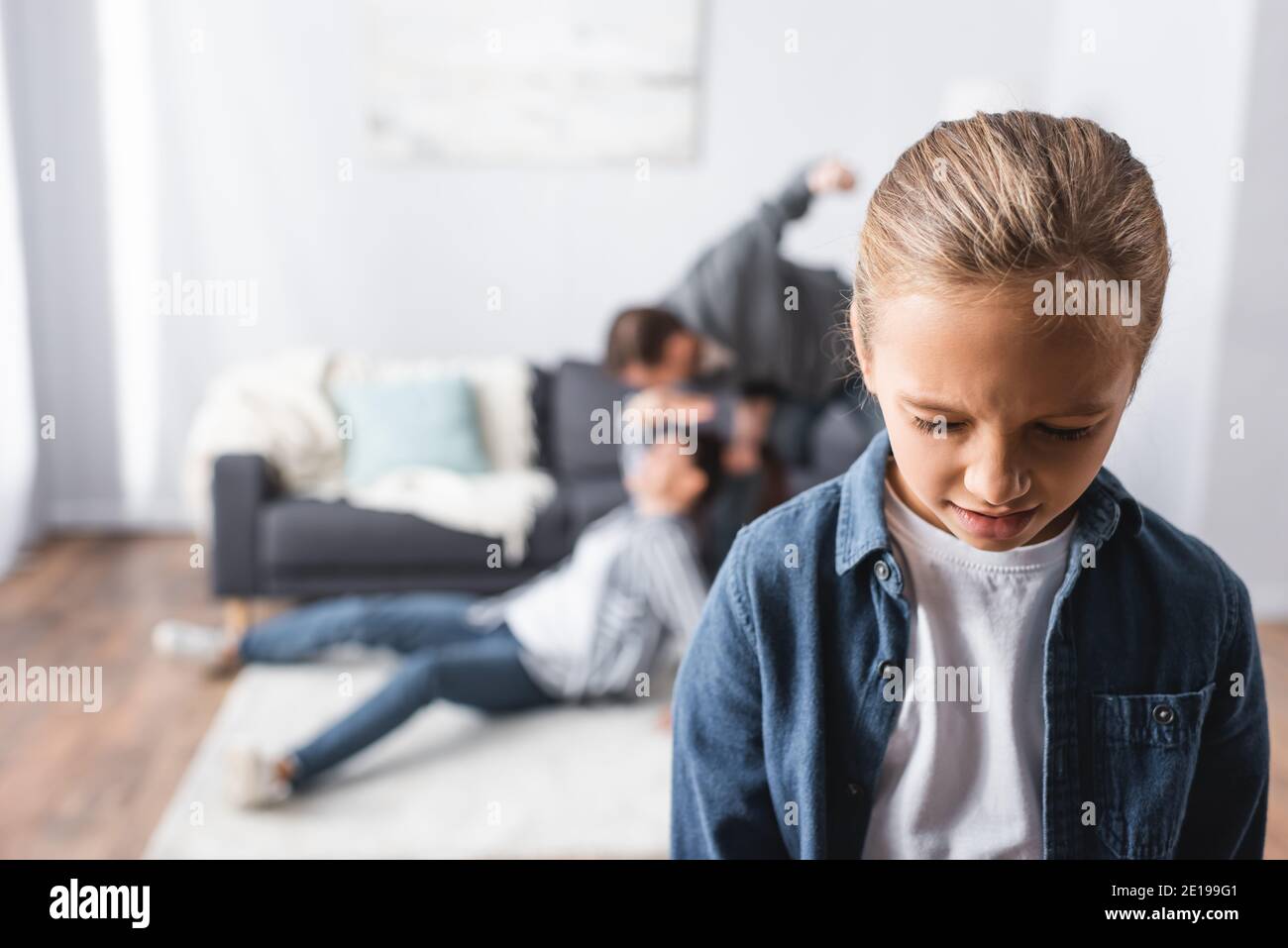 Crying girl standing near father beating mother on floor in living room on blurred background Stock Photo