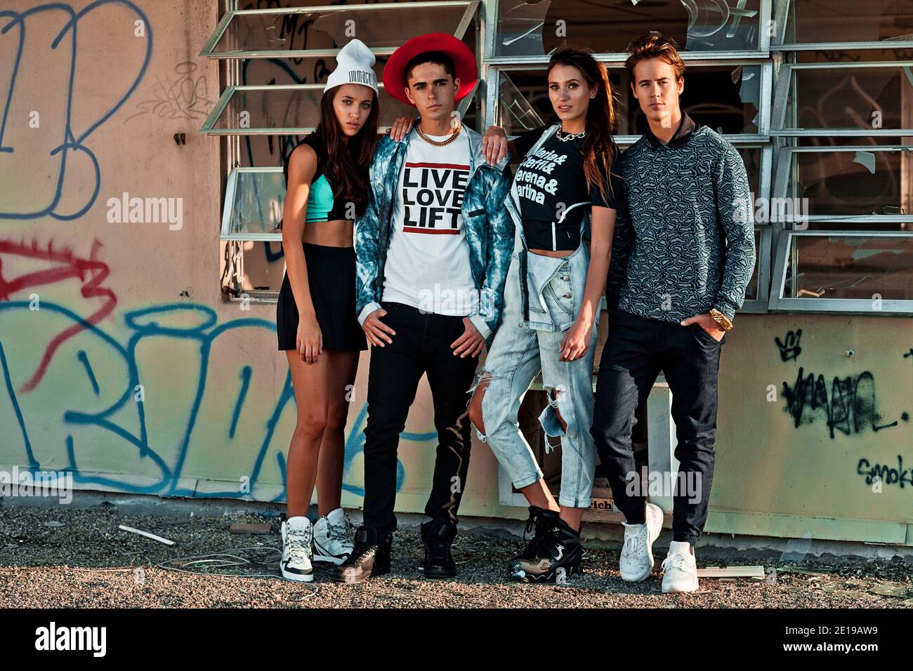 Portrait of an interracial group of 4 young adults standing in front of broken windows and graffiti sprayed walls on top of a vacant building. Stock Photo