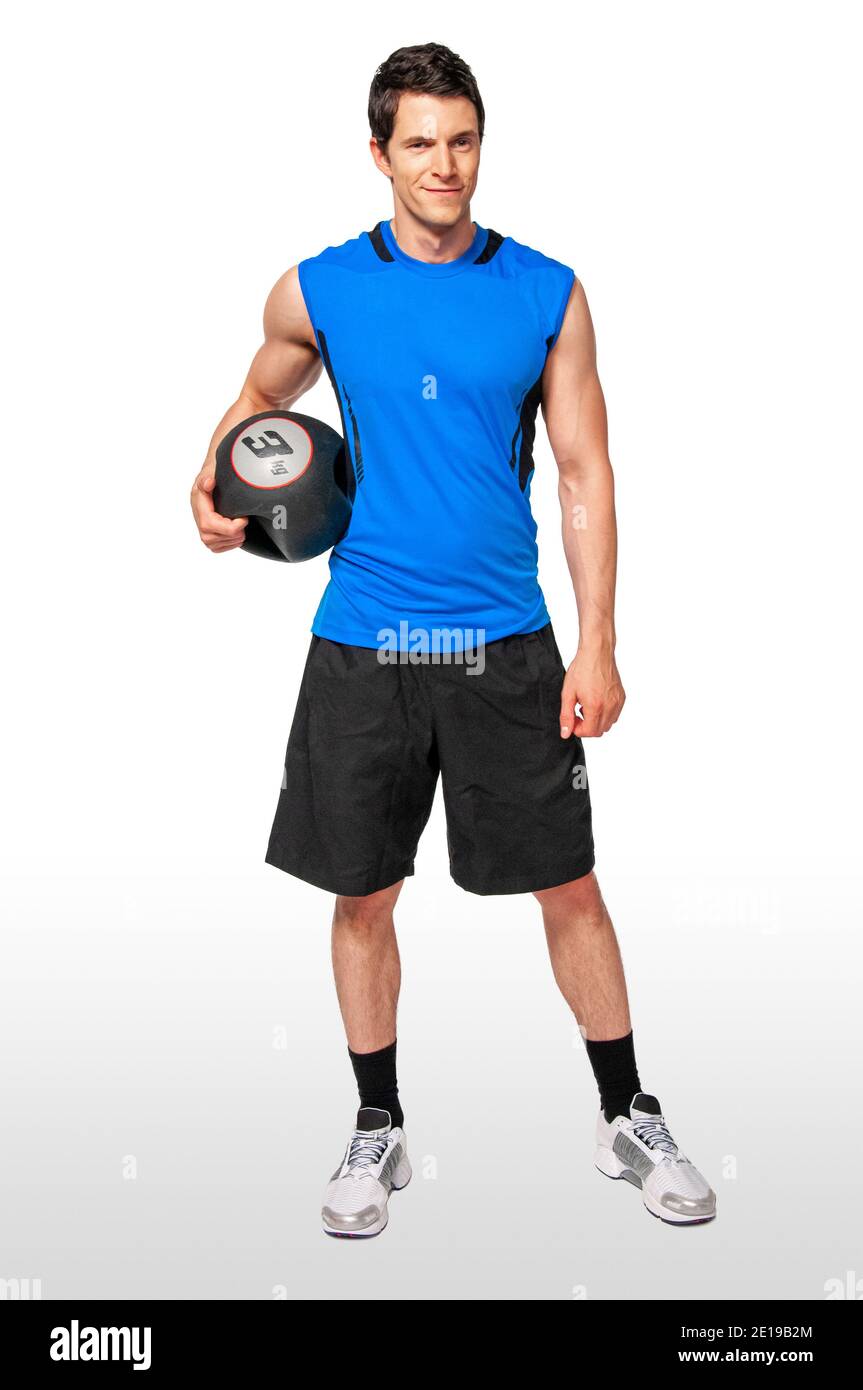 Portrait of a fit young white male athlete with short dark hair posing by himself holding a black medicine ball in a studio with a white background. Stock Photo