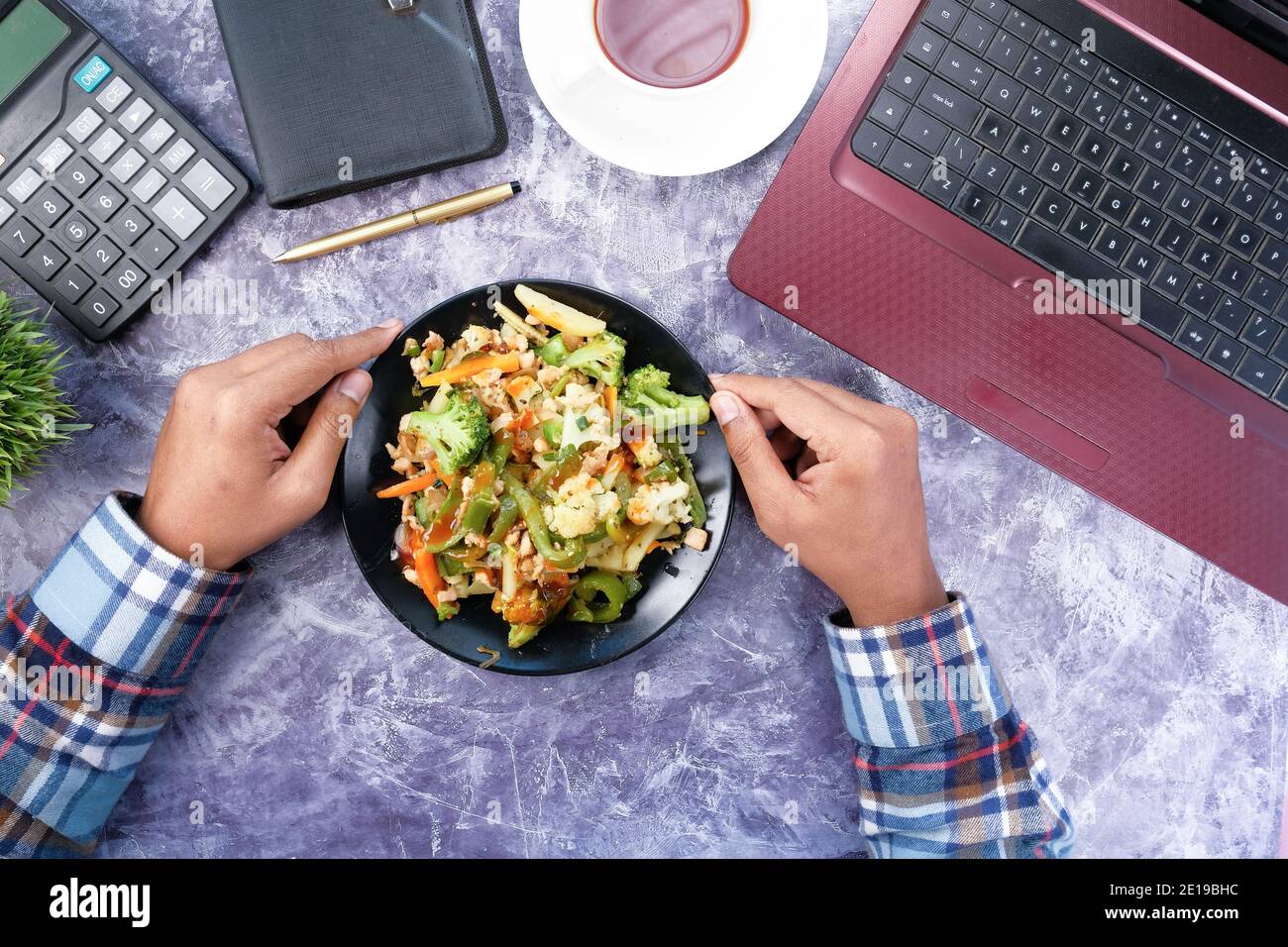 young man eating fresh salad while working on laptop  Stock Photo