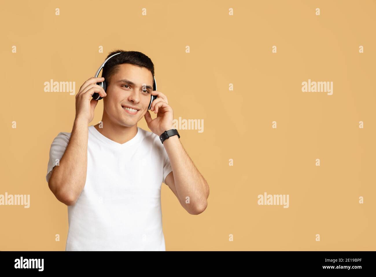 Relax, good mood and music. Happy attractive young student guy puts on modern wireless headphones Stock Photo