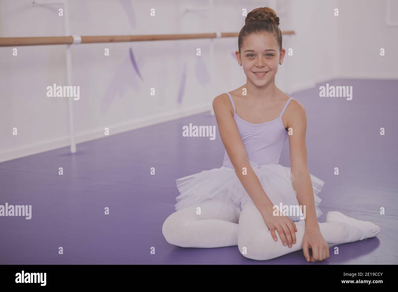 Happy beautiful young ballerina girl smiling to the camera, sitting on ...