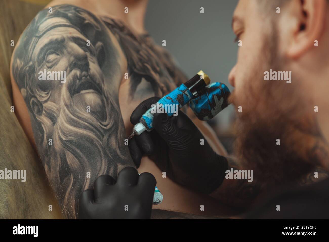 Cropped close up of a bearded tattoo artist working at his studio tattooing sleeve on the arm of his male client. Man getting tattooed by professional Stock Photo