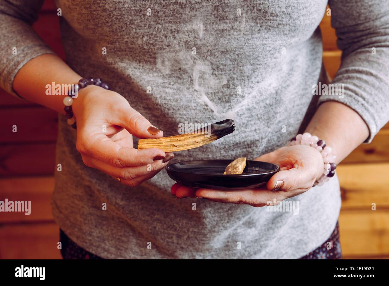 Woman hands holding and using Palo Santo wood sticks smoke for home cleansing session from old negative energy. Oily aromatic holy sacred wood sticks. Stock Photo