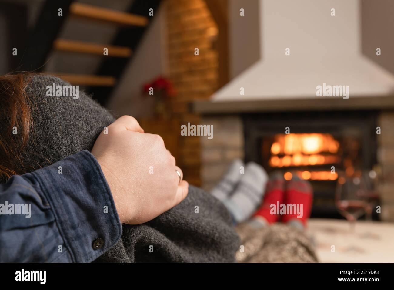 Couple in love sitting in a cozy room with fire place on a sofa with glass of wine. Family and love concept. Stock Photo