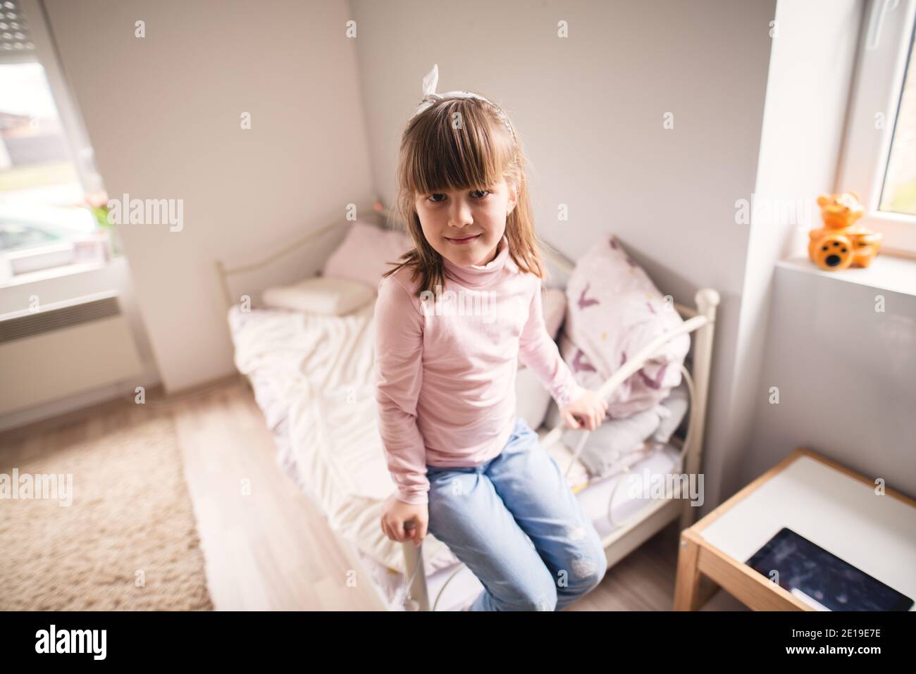 Portrait of pretty small toddler girl sitting on the edge of her bed in
