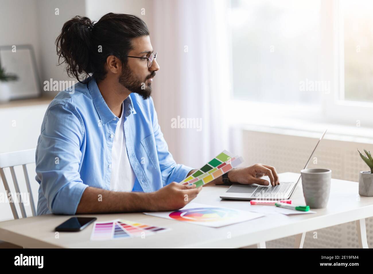 Young Eastern Freelance Designer Guy Working With Laptop And Color Swatches Stock Photo