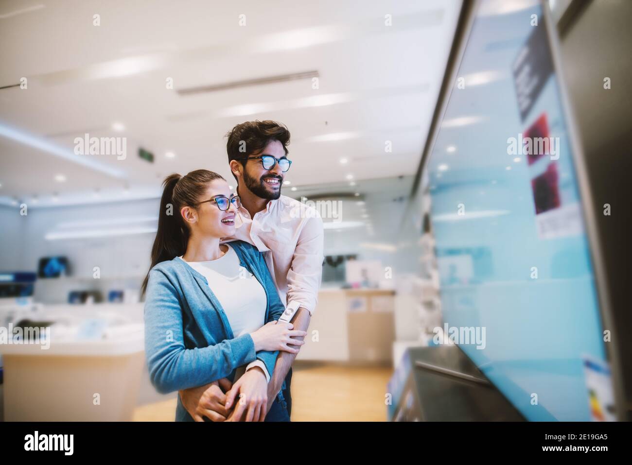 Joyful young attractive hipster couple checking out plasma TVs in the electronic store. Stock Photo