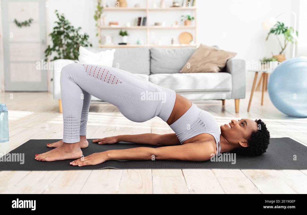 Side view of athletic black lady doing abs exercise, standing in yoga pose during her home workout Stock Photo