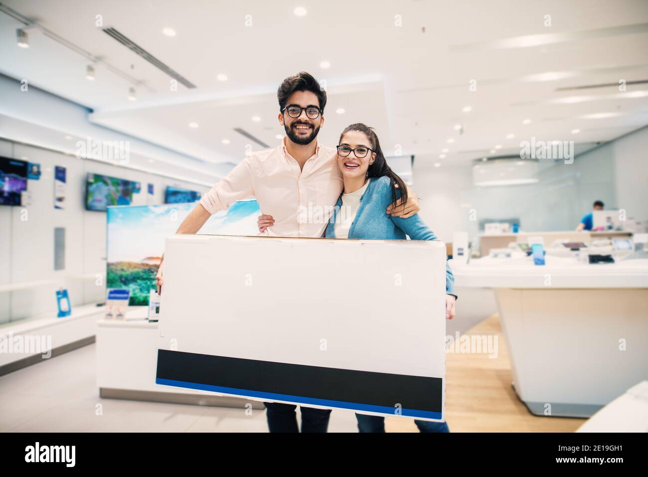 Happy young lovely modern couple with bought big tv in the electronic store. Stock Photo