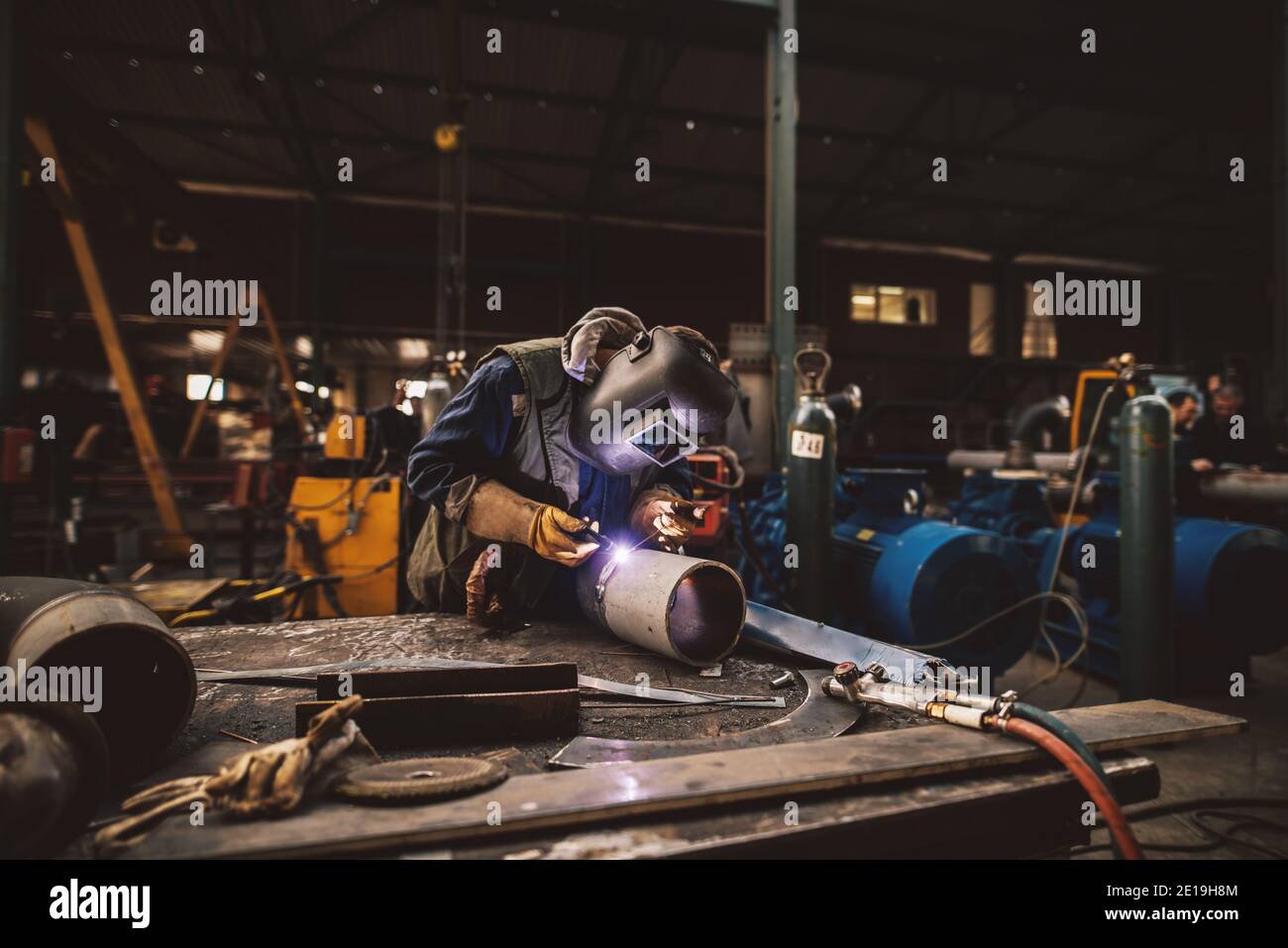 Welder in protective uniform and mask welding metal pipe on the