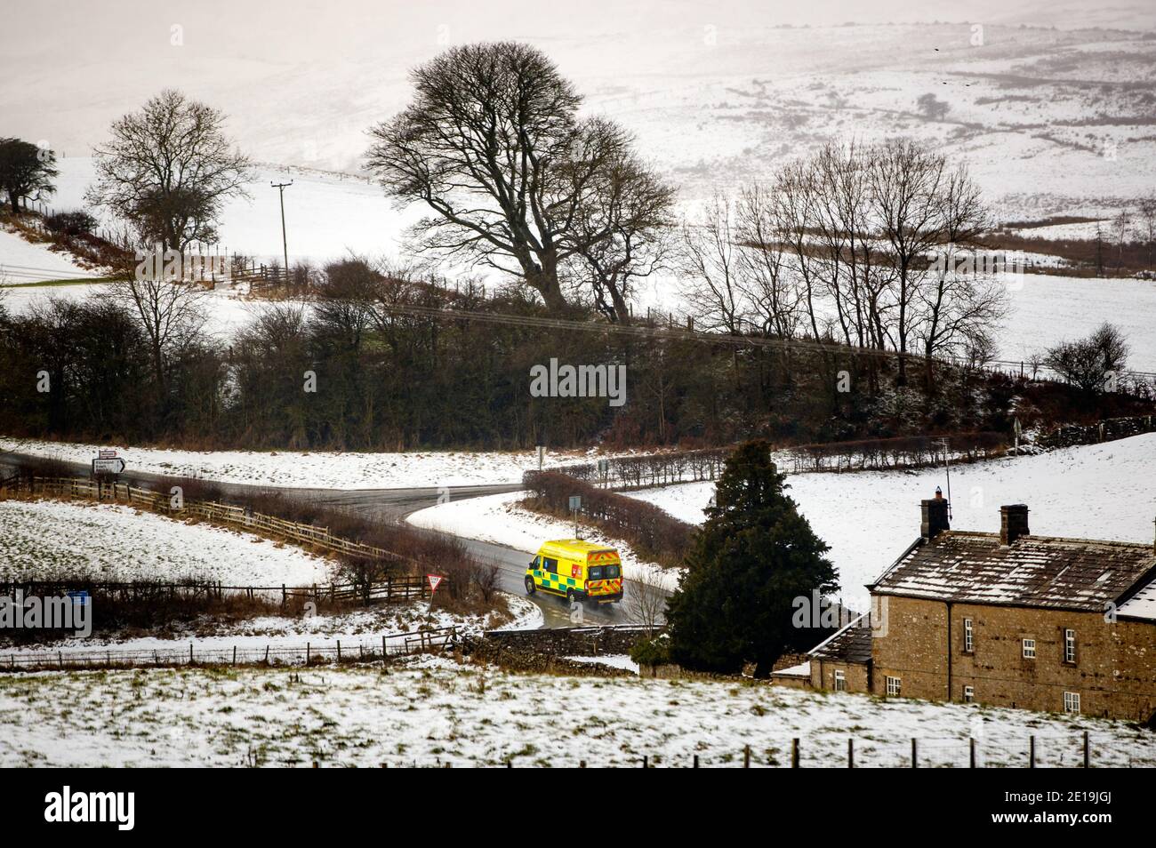 An ambulance makes its way down a country lane in the snow covered countryside near Bellerby, North Yorkshire. Stock Photo