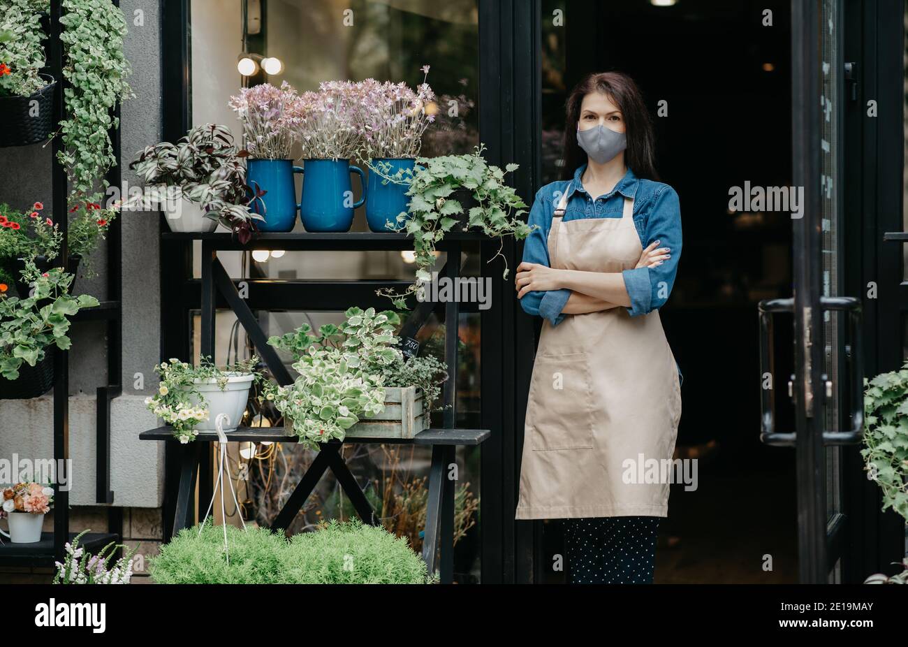 Decorative plants, gardening and floristry. Confident lady in apron and protective mask with crossed arms Stock Photo