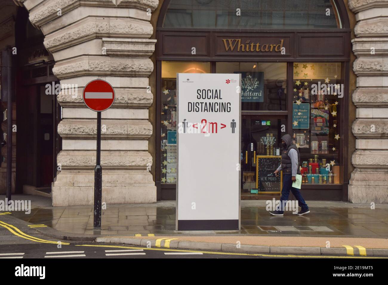 A man wearing a protective face mask walks past a social distancing sign on Regent Street in London as England imposes the third national lockdown. Stock Photo