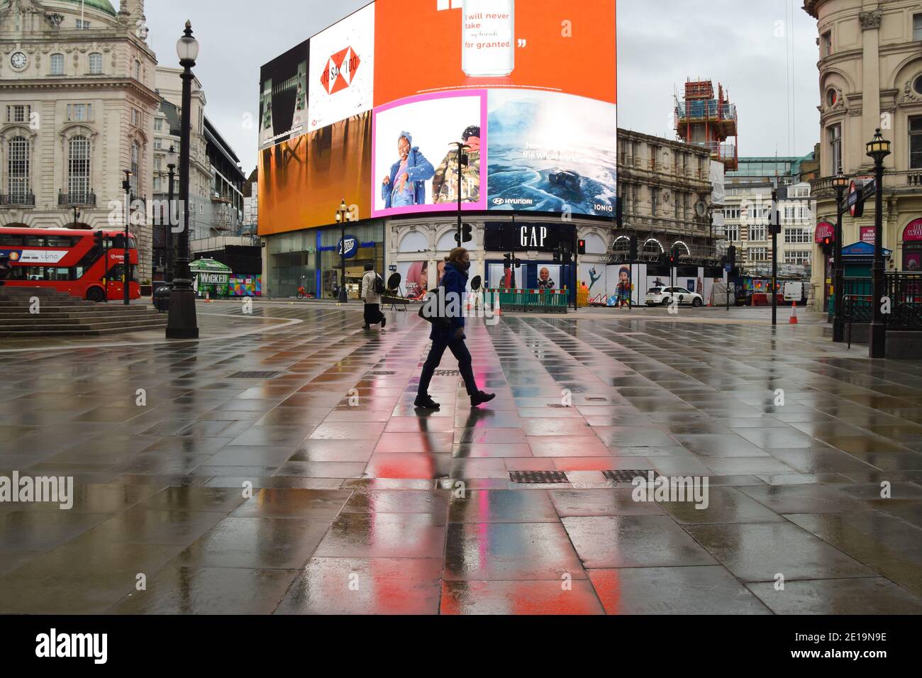 A woman wearing a protective face mask walks along a deserted Piccadilly Circus in London as England imposes the third national lockdown. Stock Photo