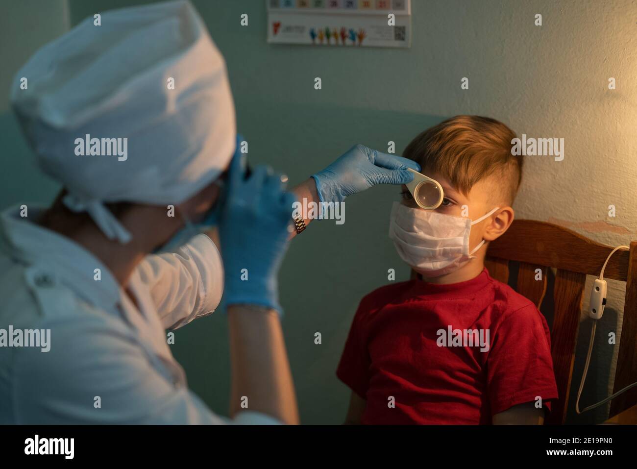 Eye diagnostic examination and specialist consultation to a boy. Doctor and boy wearing protective mask during outbreak of the coronavirus. City Stock Photo