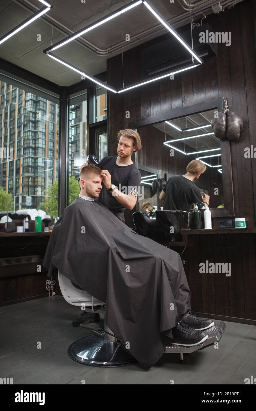 Vertical full length shot of a professional barber blow drying hair of a male client Stock Photo