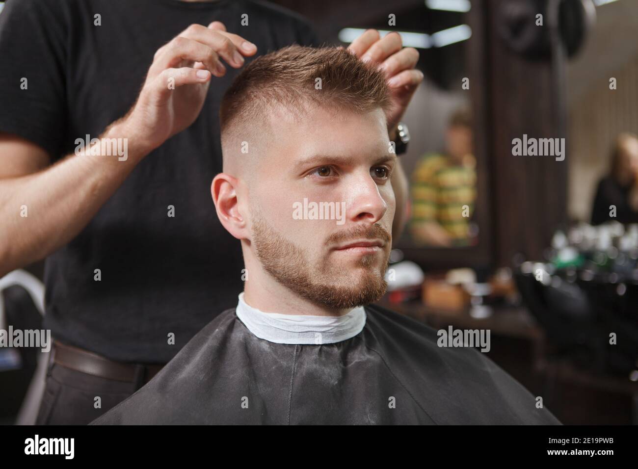 Unrecognizable barber styling hair of handsome young bearded man Stock Photo