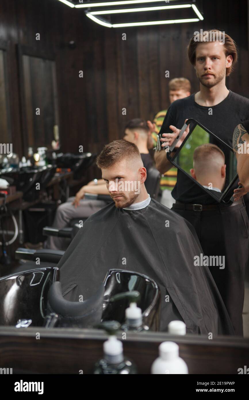 Vertical shot of a man examining his new haircut in the mirror at barbershop Stock Photo