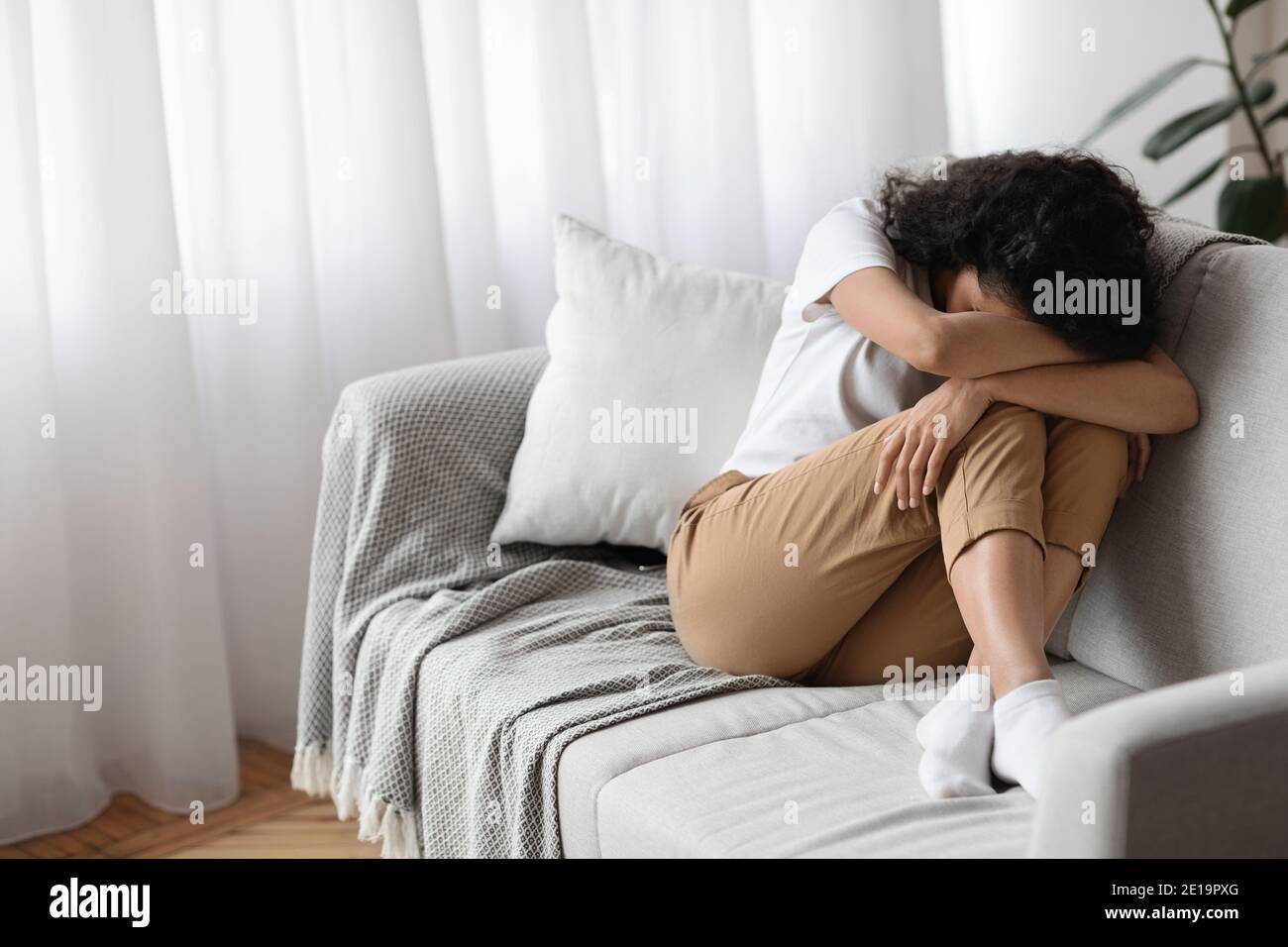 Depressed brunette woman sitting on couch alone, crying Stock Photo