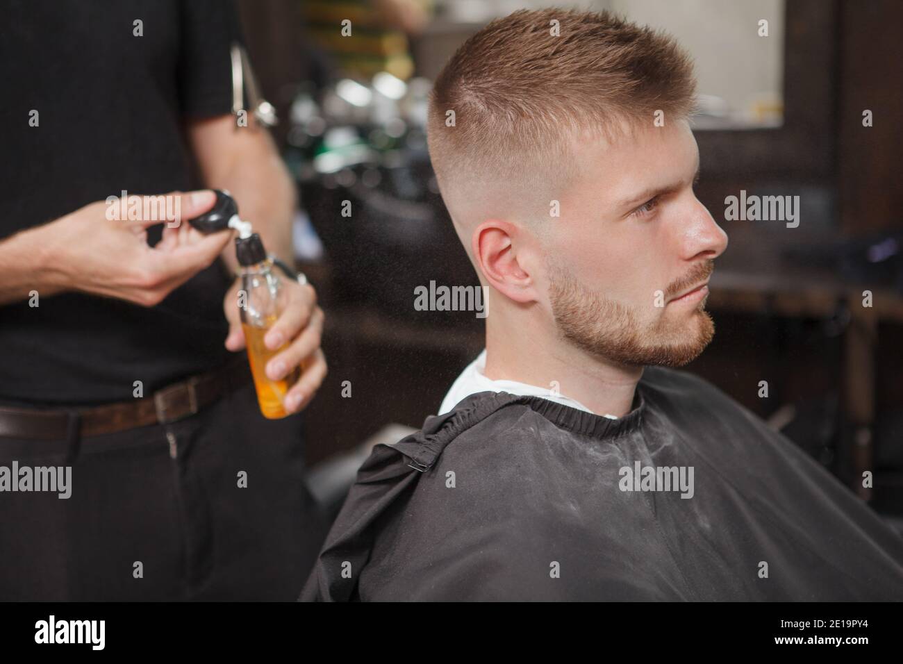 Unrecognizable barber spraying cologne on his male customer after shaving him and giving a new haircut Stock Photo
