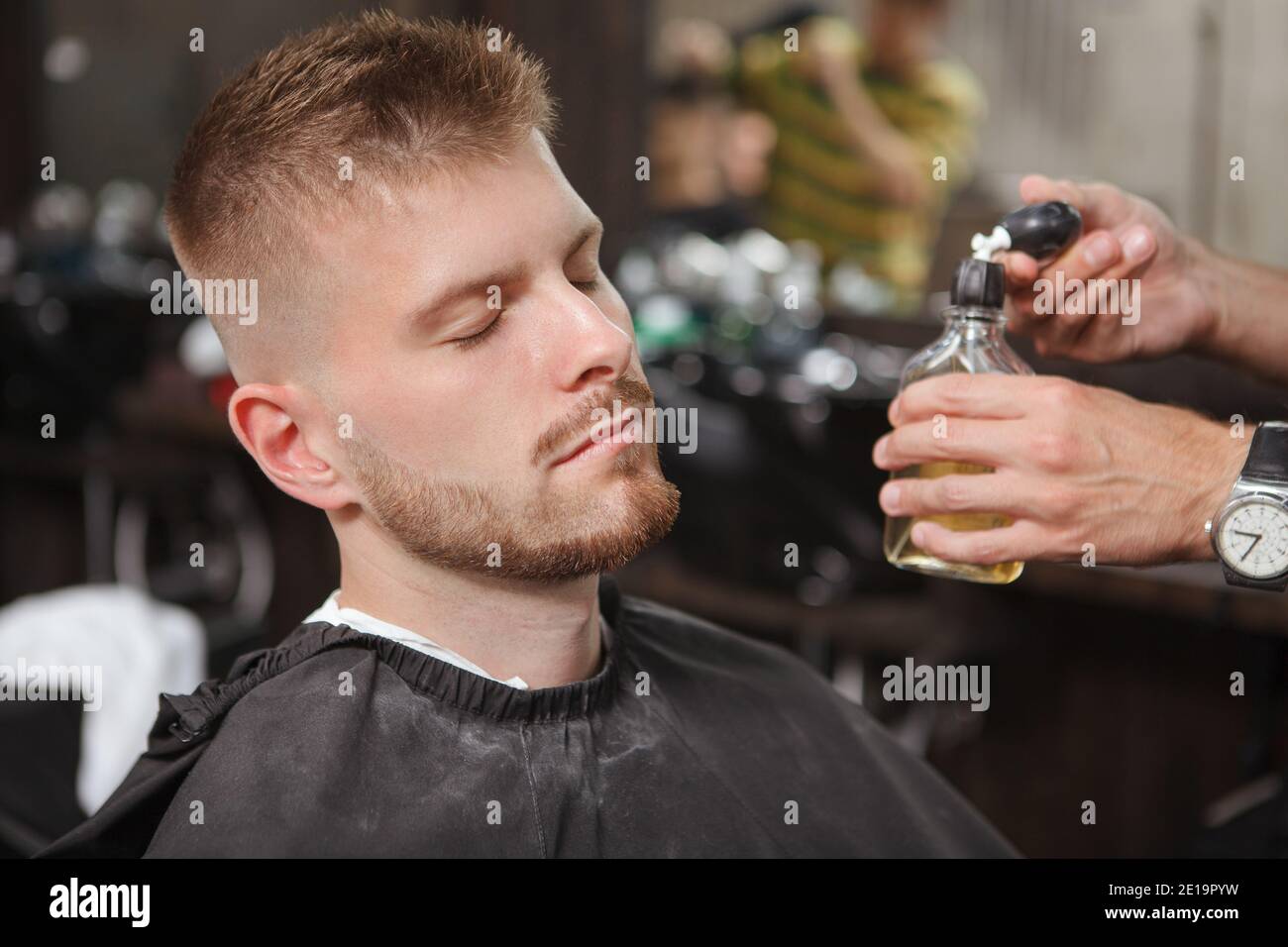 Close up of a male clietn being sprayed with cologne at the barbershop after getting a new haircut and shaving beard Stock Photo