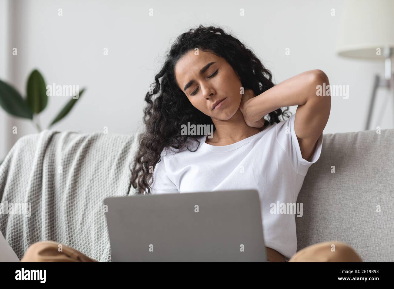 Brunette woman having pain in neck while working with laptop Stock Photo