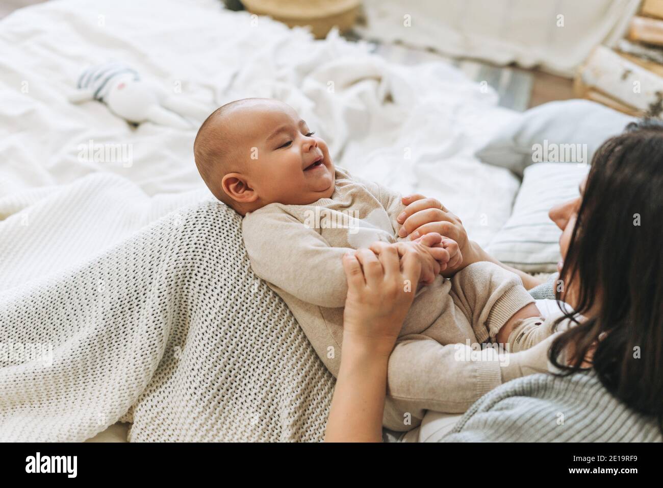 Young mother having fun with cute baby boy on bed, natural tones ...