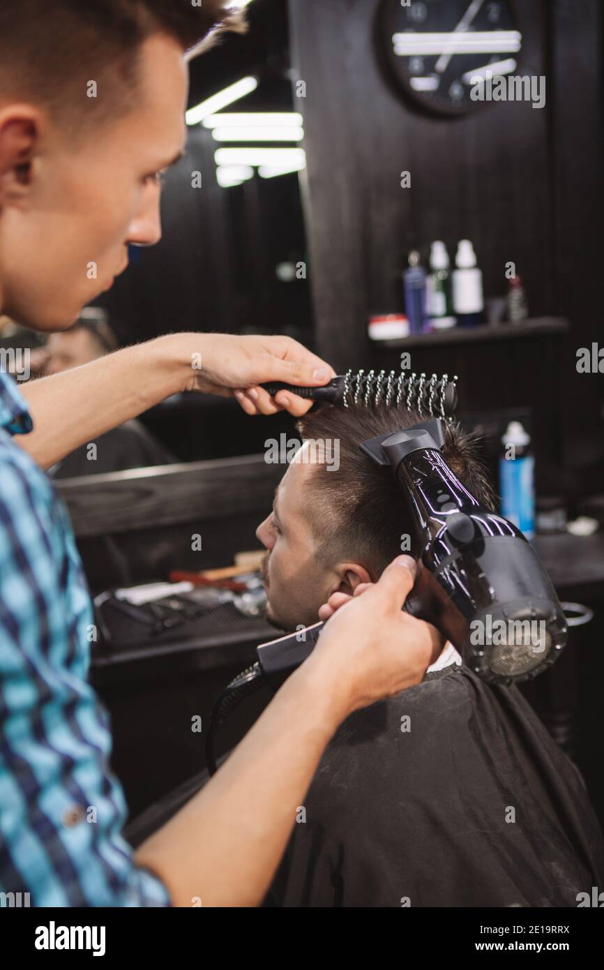 Vertical shot of a man having his hair blow dried by professional barber. Cropped shot of a hairstylist blow drying hair of a male customer after givi Stock Photo