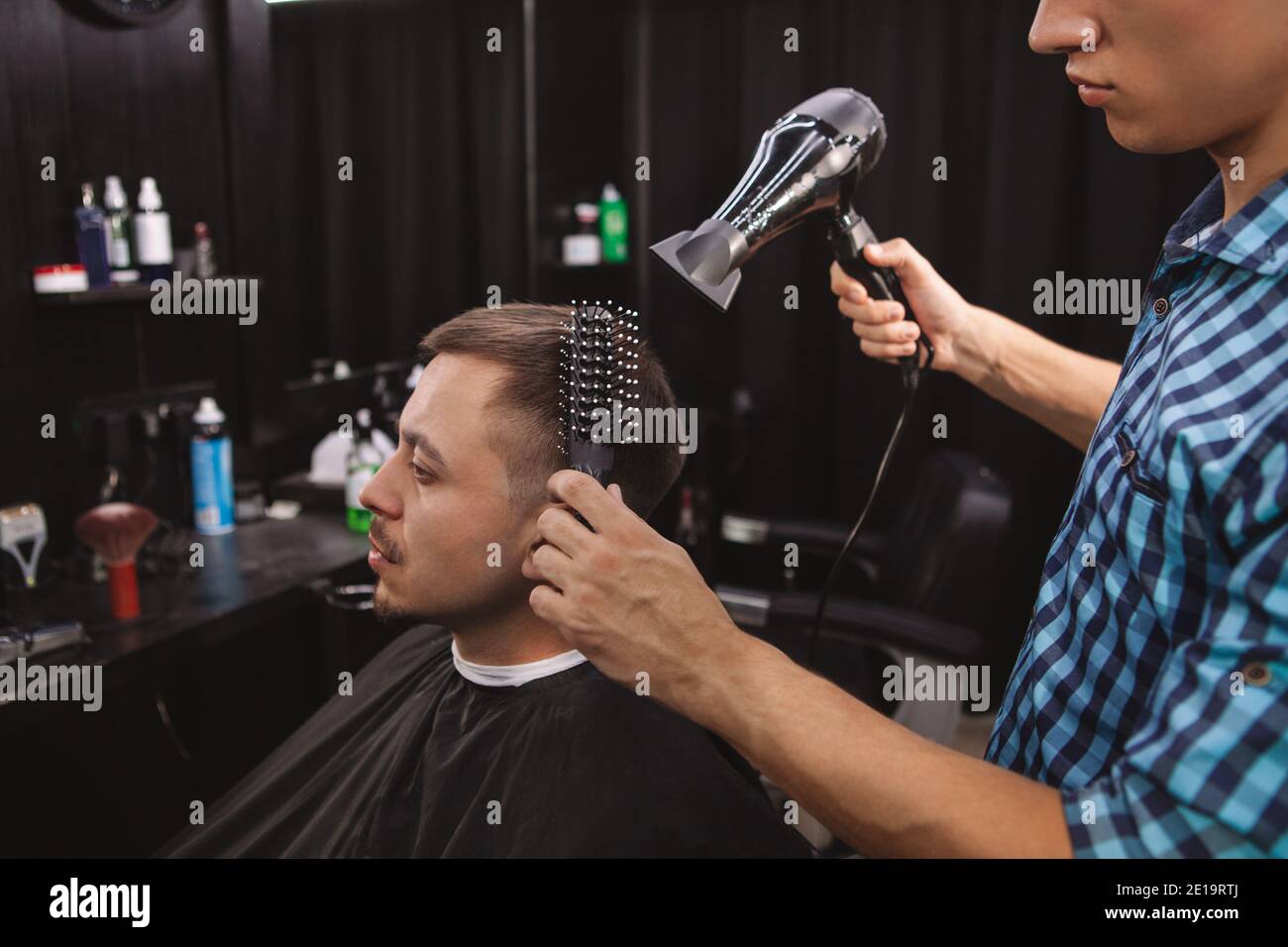 Mature man enjoying getting a new hairstyle by professional barber. Hairstylist blow drying hair of a male client. Barbershop, hair care concept Stock Photo