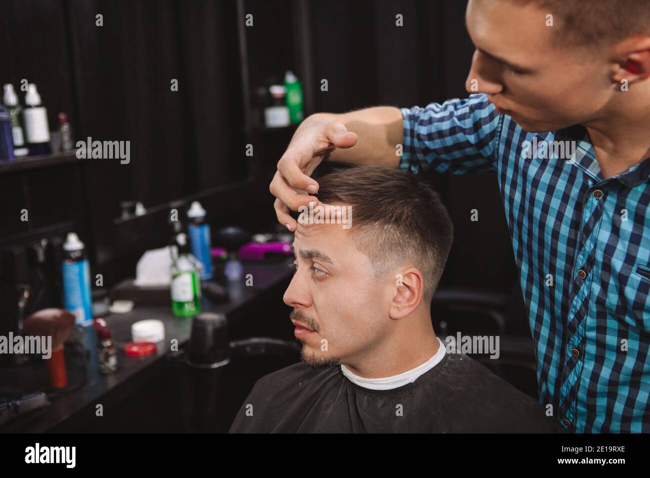 Cropped shot of a mature man looking in the mirror while barber styling his hair. Professional hairstylist working at the barbershop, styling hair of Stock Photo