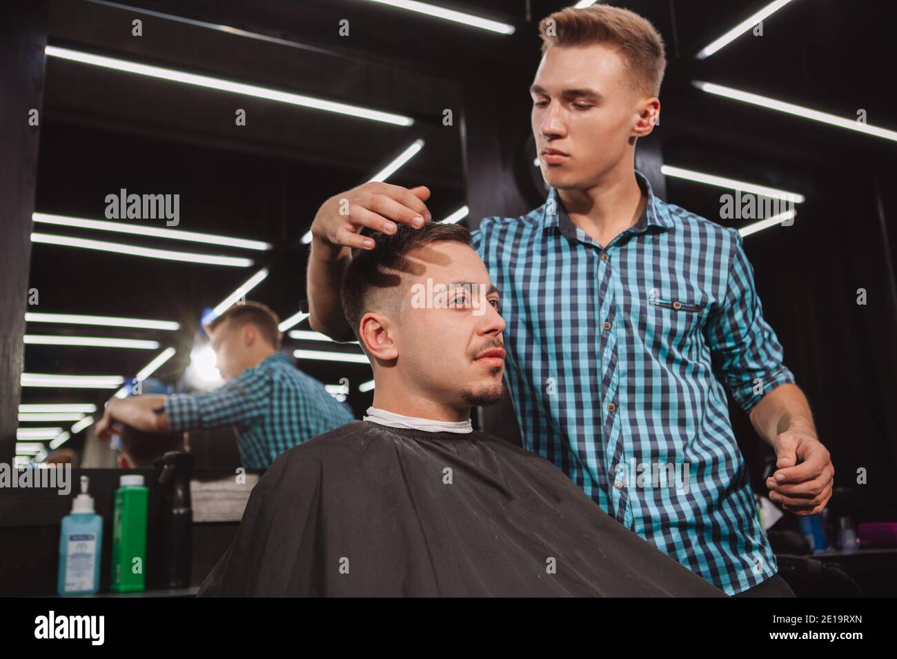 Mature man getting his hair styled by professional barber. Young handsome hairstylist working at his barbershop, styling hair of a male customer Stock Photo