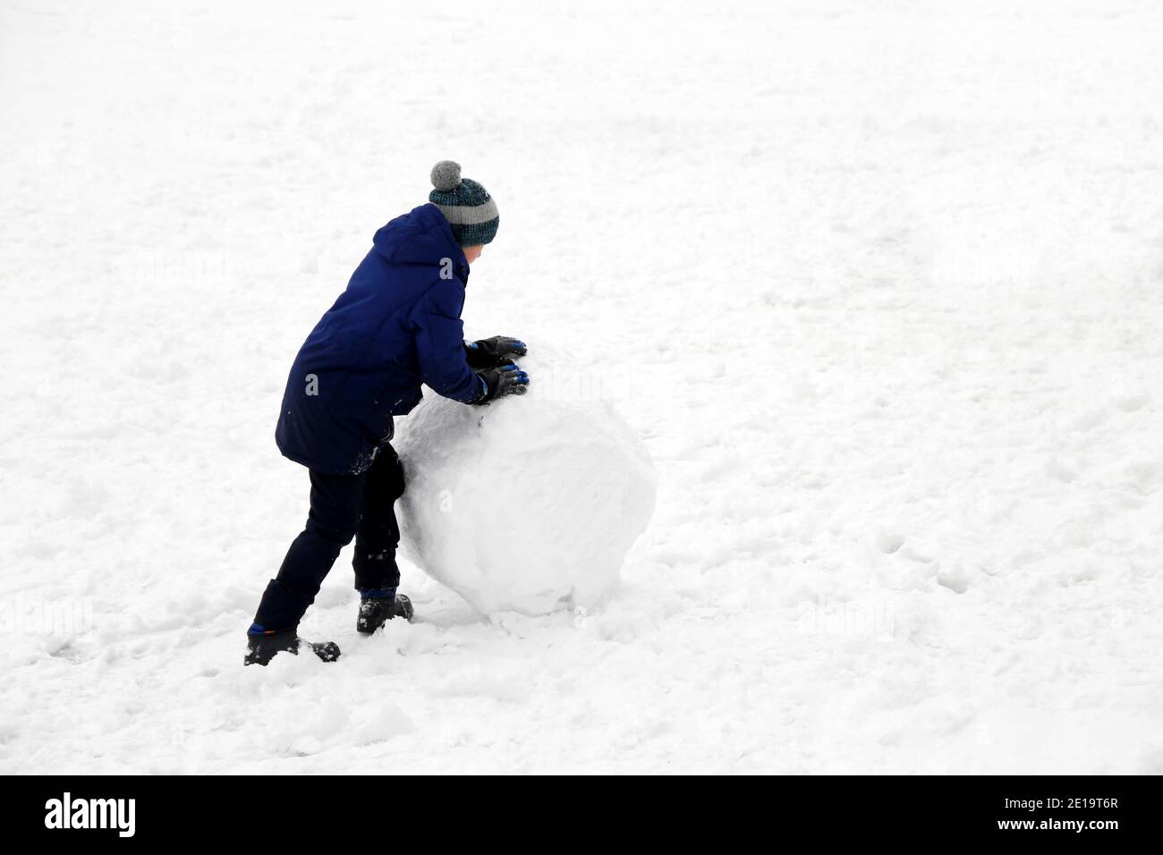 Child rolls a snowball on a street. Winter leisure, boy making a snowman Stock Photo