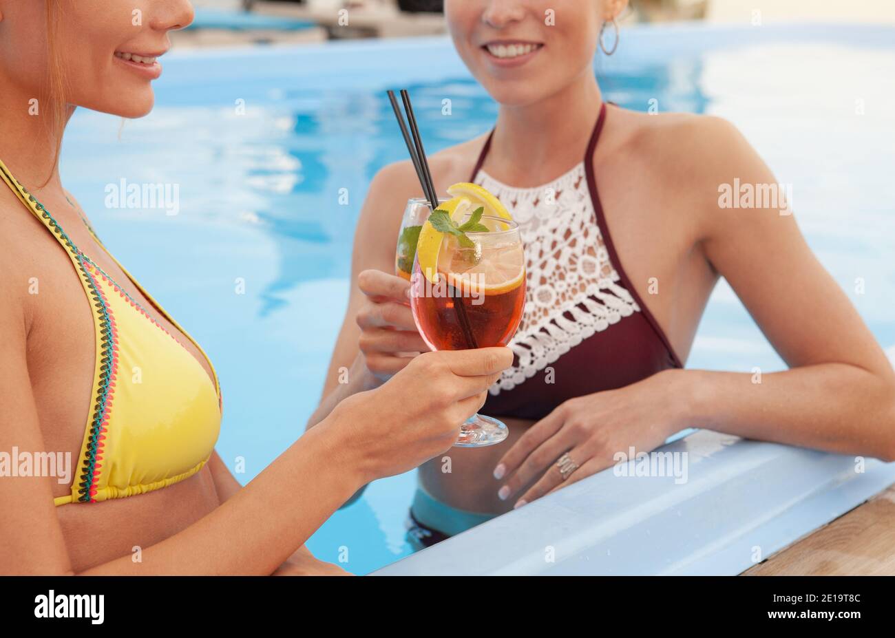 Cropped shot of two happy beautiful women enjoying cocktails at the swimming pool. Cheerful female friends relaxing at the poolside, having drinks tog Stock Photo