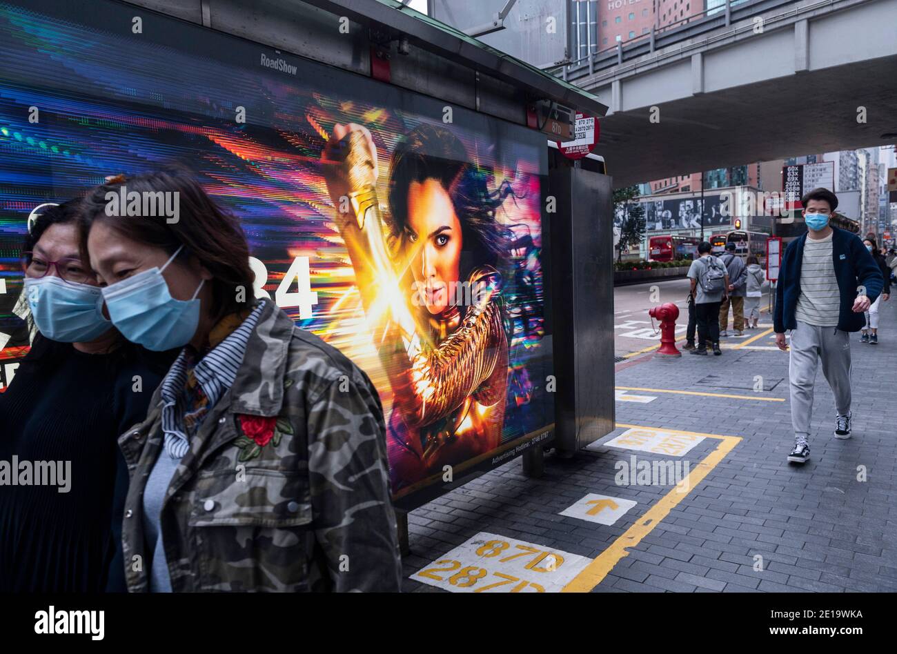 Pedestrians wearing masks walk past an advertisement billboard from Warner Bros Official Site and DC comics character Wonder Woman 1984 movie in Hong Kong. Stock Photo